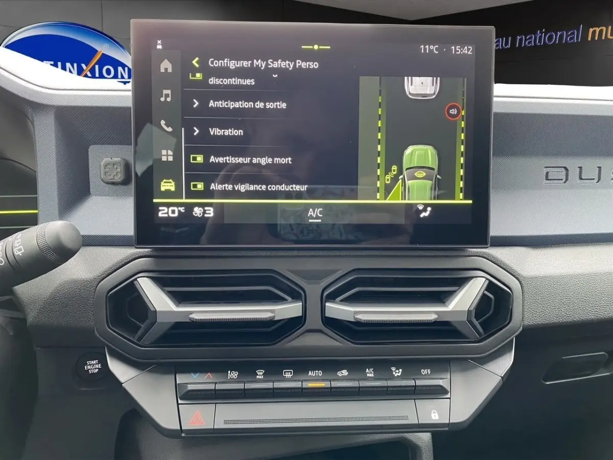 Vue rapprochée de l'écran tactile central et des aérateurs hexagonaux du tableau de bord gris foncé du Dacia Duster 2025.