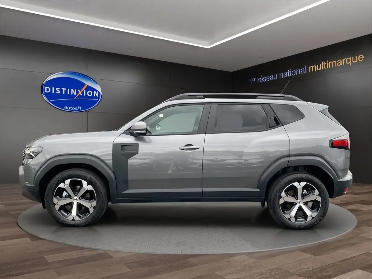 Vue latérale droite du Dacia Duster Journey Hybrid 140 gris foncé avec jantes alliage distinctives en showroom.