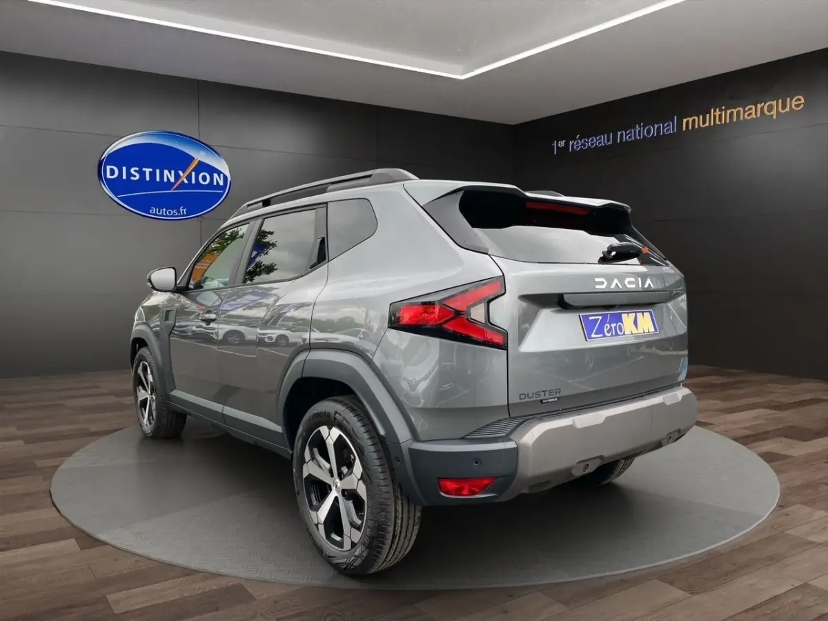 Vue 3/4 arrière droite d'un Dacia Duster gris foncé avec jantes alliage et barres de toit noires en showroom.