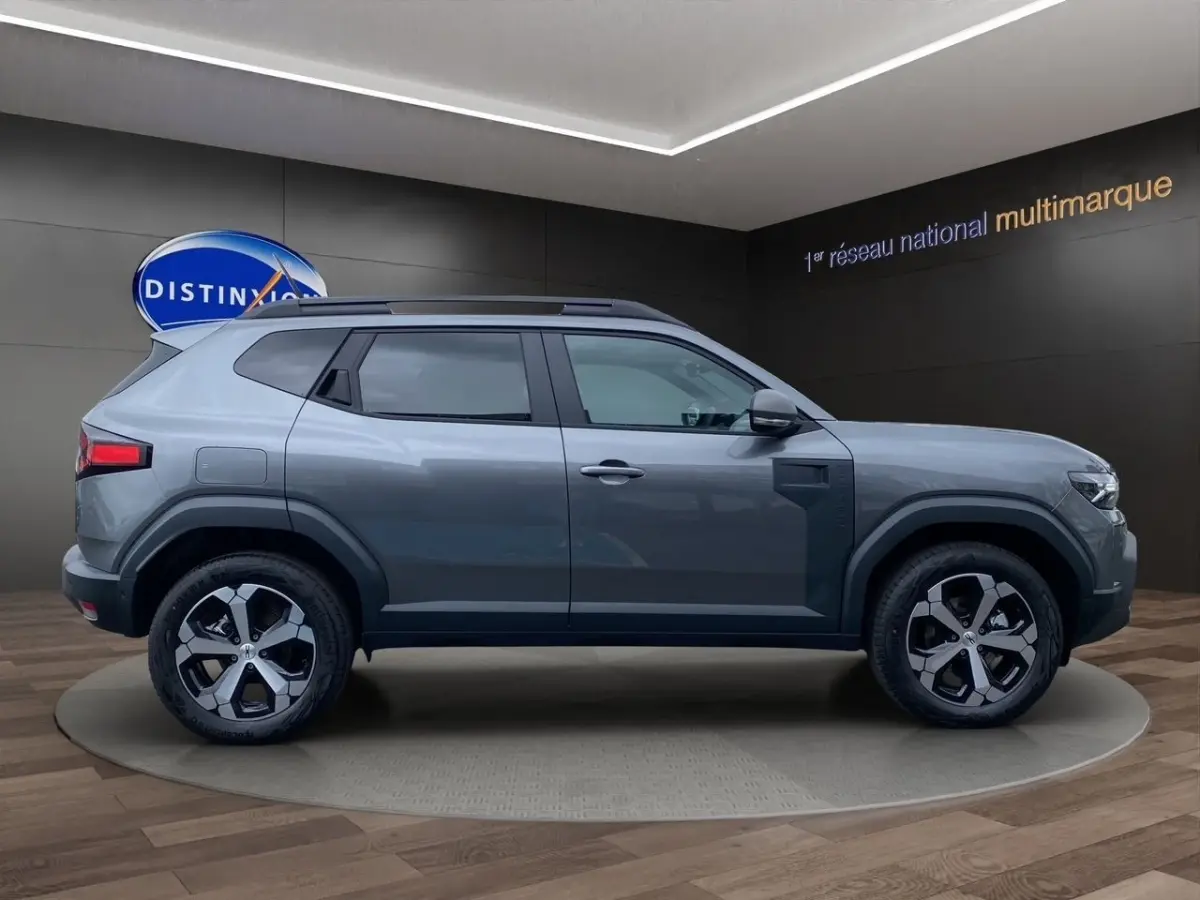 Profil droit du Dacia Duster Journey Hybrid 140 gris foncé avec jantes alliage et barres de toit noires.