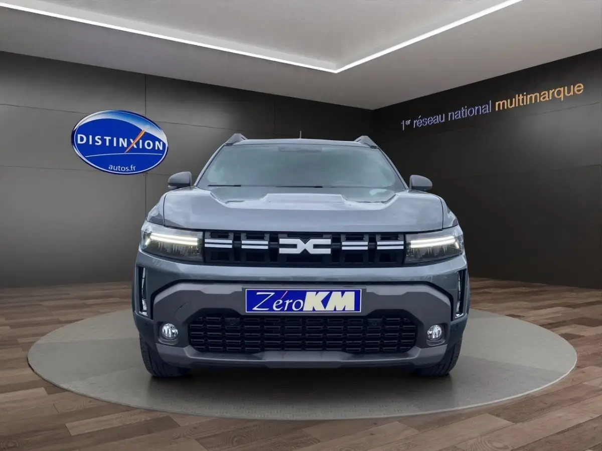 Vue frontale d'un Dacia Duster Journey Hybrid 140 gris foncé avec calandre noire et feux LED allumés.