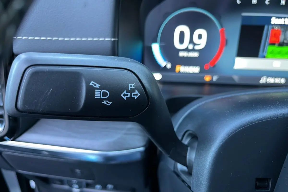 Gros plan sur la manette de clignotants et feux du Ford Ranger 3.0 V6 Platinum, avec tableau de bord numérique en arrière-plan.