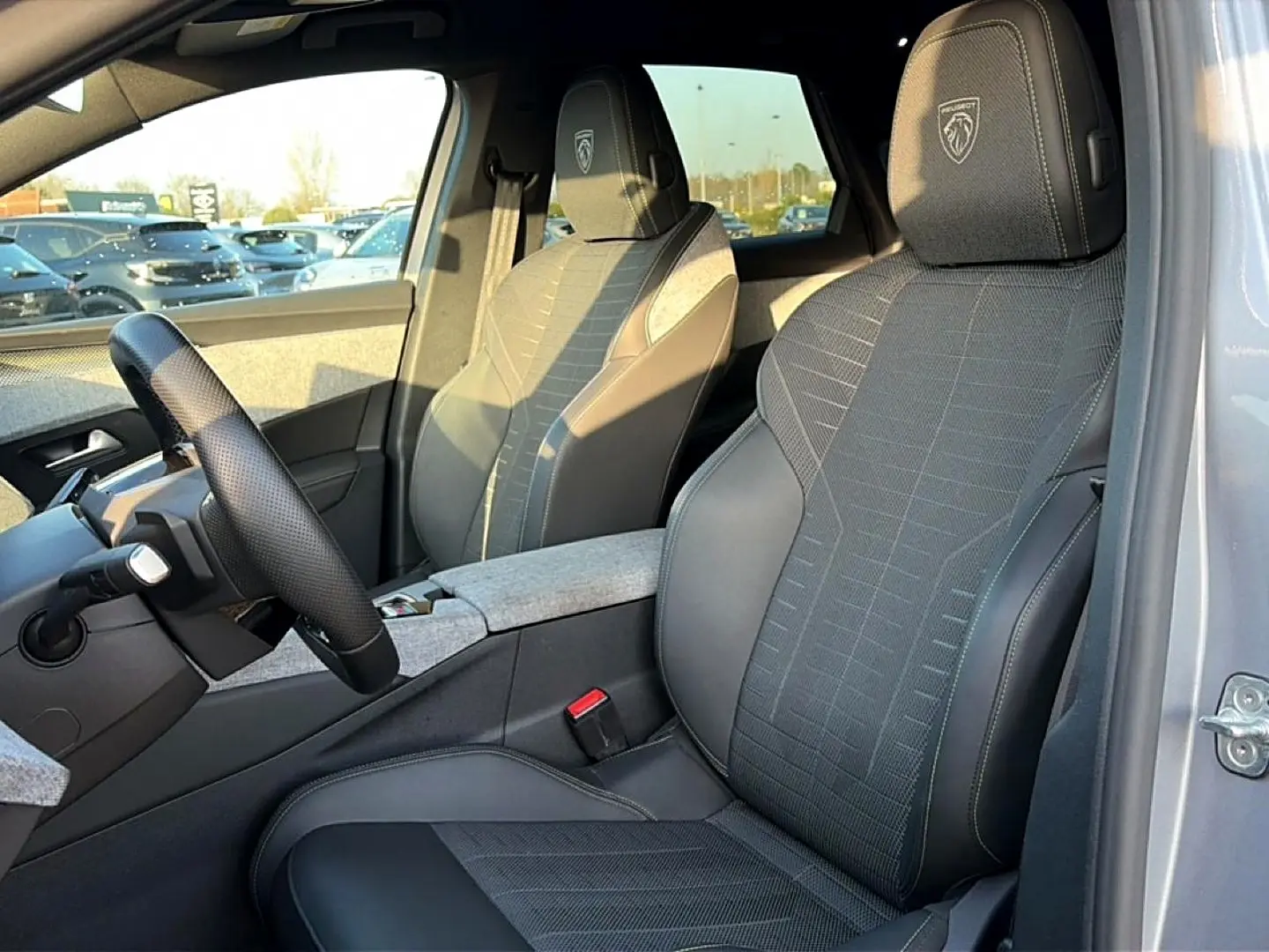 Vue intérieure côté conducteur du Peugeot 3008 gris 2025, sièges sport avec logo Peugeot brodé sur appuie-tête.