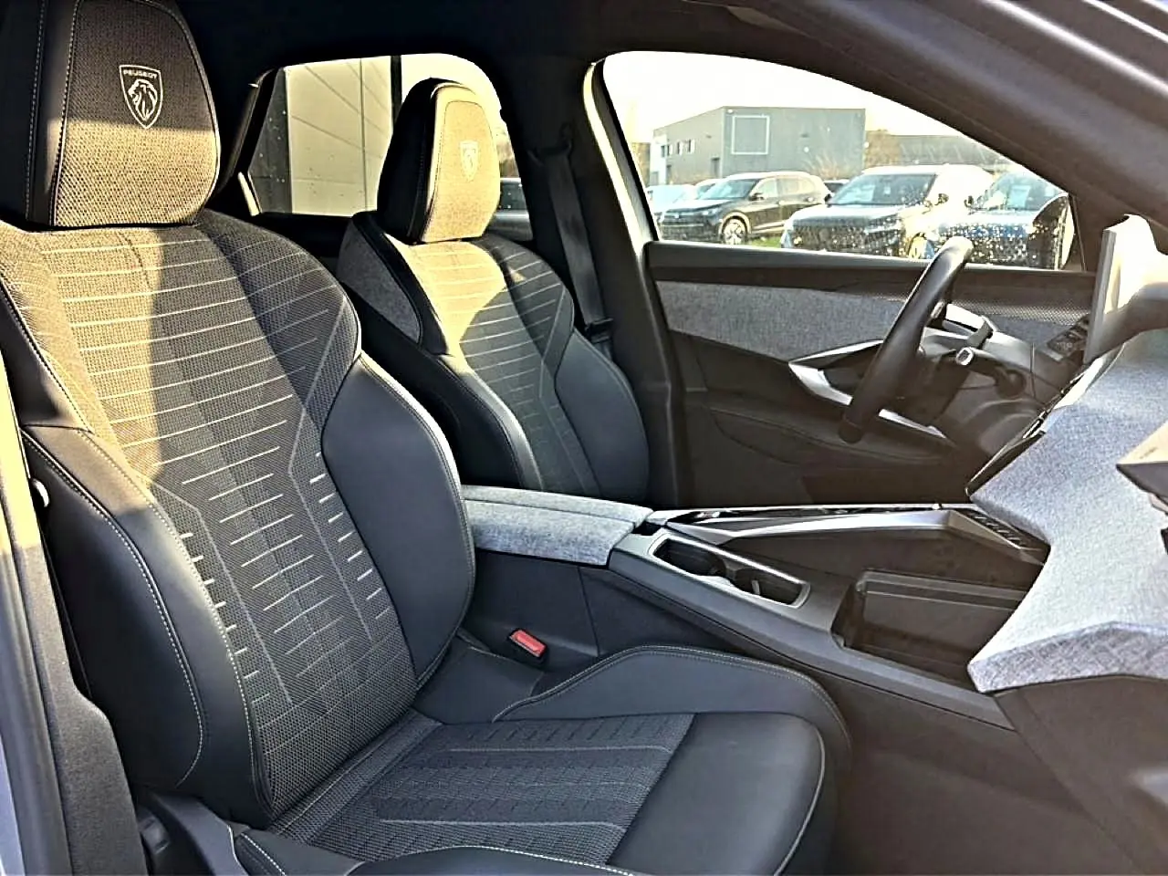Vue intérieure côté conducteur du Peugeot 3008 gris 2025, sièges tissu et cuir avec logo Peugeot brodé sur appuie-tête.