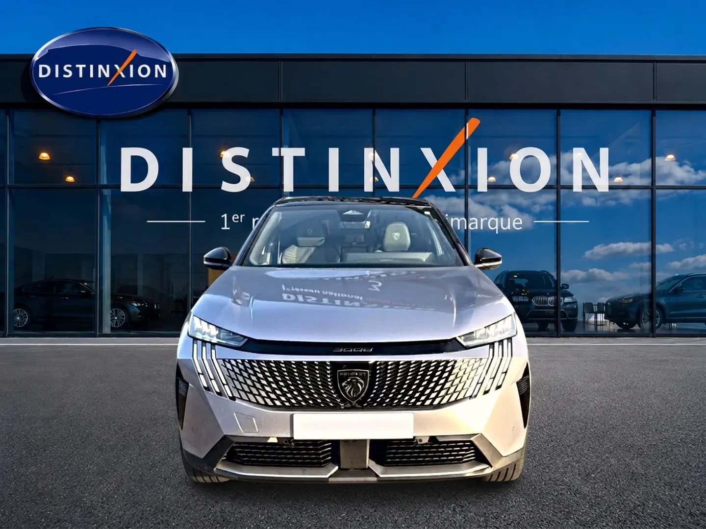 Vue frontale d'un Peugeot 3008 gris 2025 avec calandre distinctive et phares LED, devant une vitrine Distinxion.