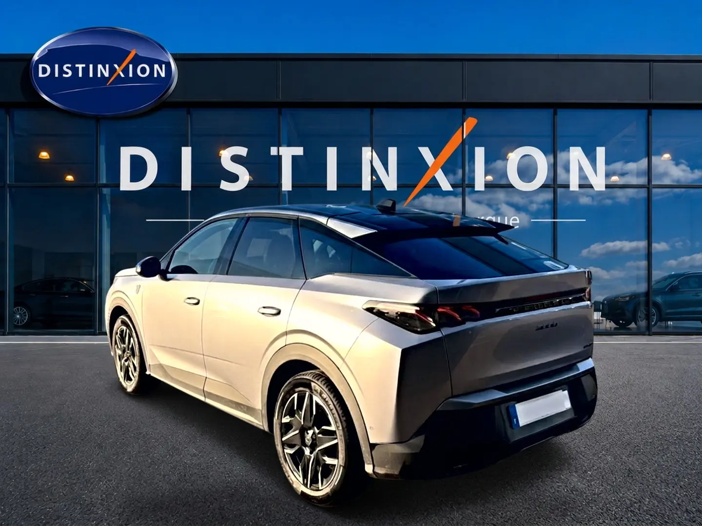 Vue 3/4 arrière droite d'un Peugeot 3008 gris 2025 avec toit noir et jantes alliage devant une vitrine Distinxion.