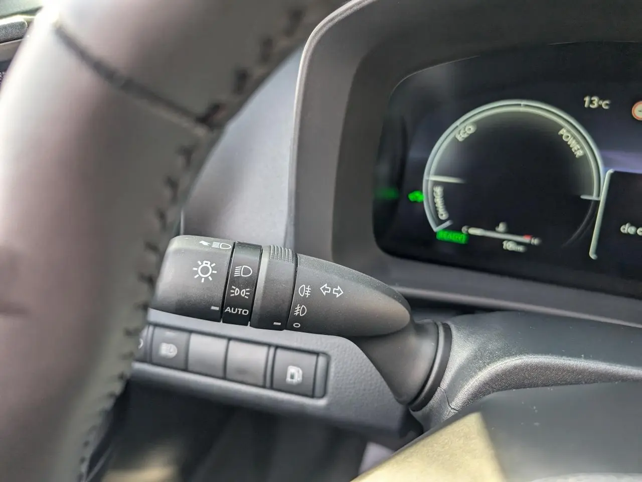 Gros plan sur la commande des feux et clignotants à gauche du volant du Toyota C-HR blanc 2024, tableau de bord numérique visible.