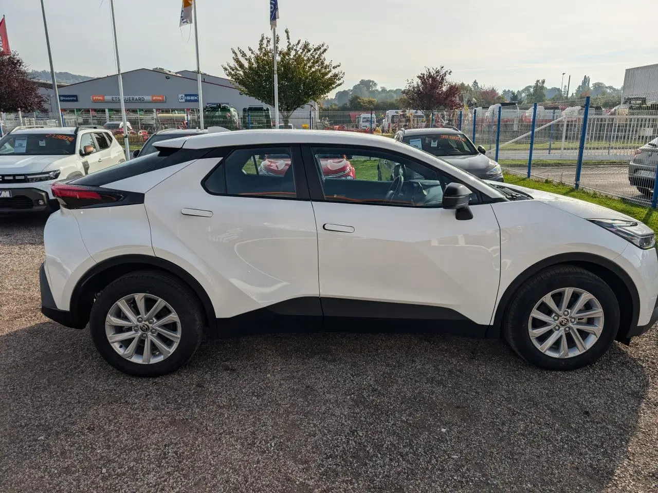 Profil côté gauche du Toyota C-HR 1.8 Hybrid blanc 2024, avec lignes anguleuses et toit noir contrastant.