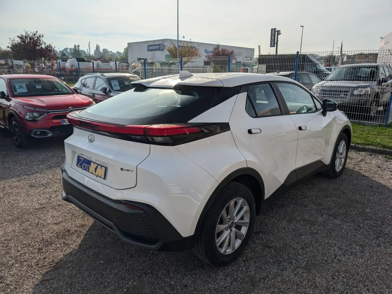 Vue 3/4 arrière droite du Toyota C-HR blanc 2024 avec feux arrière reliés et toit noir contrastant.