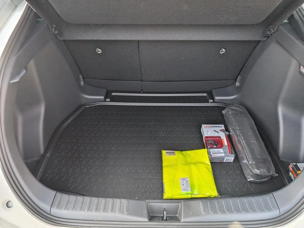 Coffre ouvert vu de l'arrière d'un Toyota C-HR blanc 2024, avec tapis de coffre et accessoires de sécurité visibles.