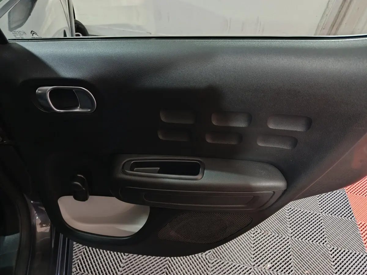 Vue intérieure côté gauche de la porte avant gris foncé de la Citroën C3 2024 avec poignée et habillage noir et blanc.