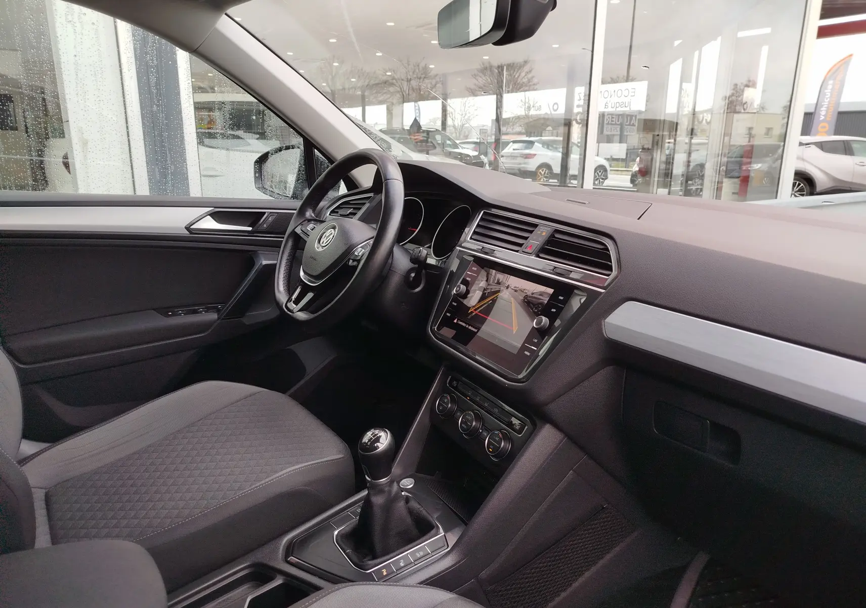 Vue intérieure côté conducteur du Volkswagen Tiguan 2019 noir, avec tableau de bord moderne et écran tactile affichant la caméra de recul.