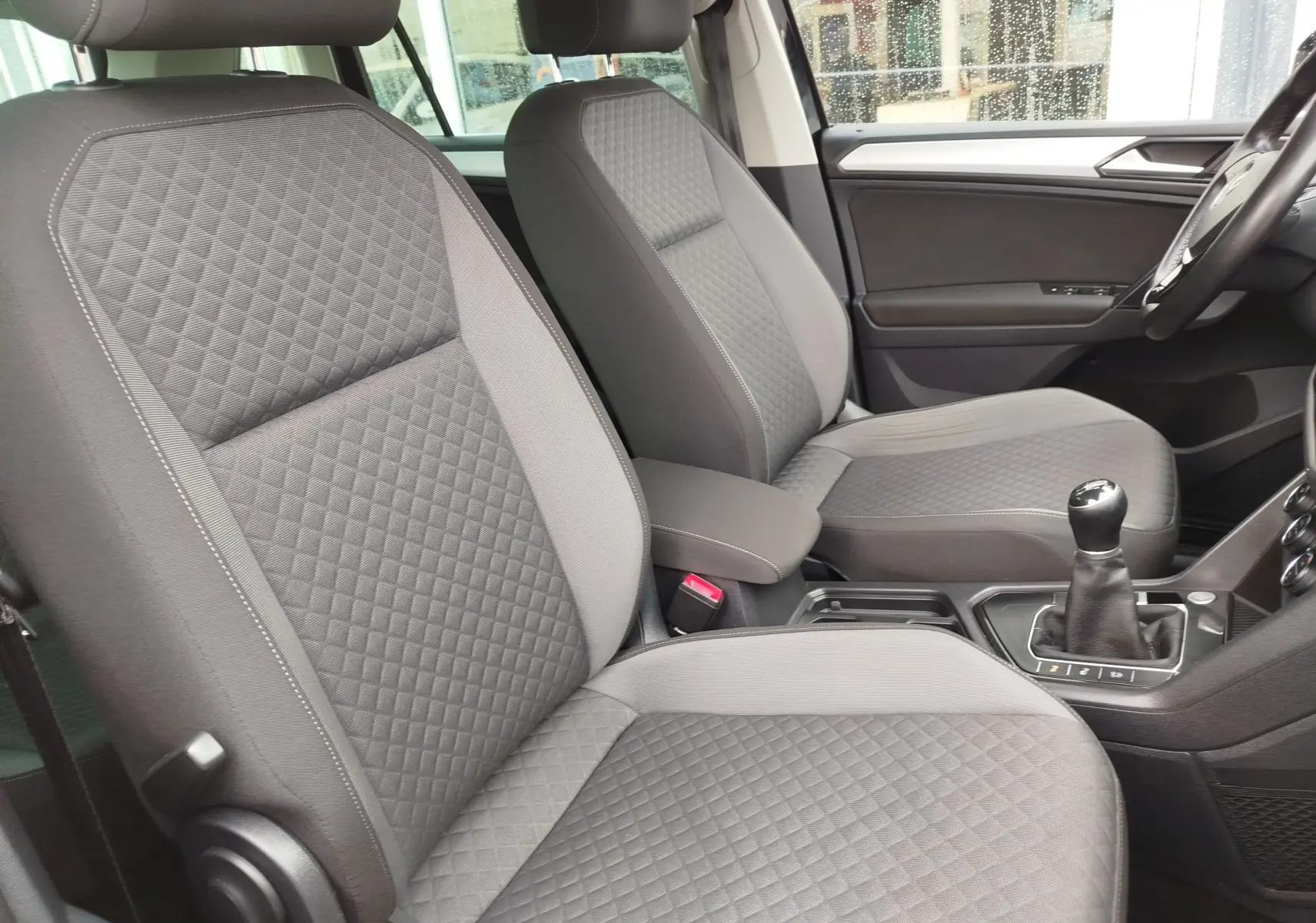 Vue intérieure côté gauche du Volkswagen Tiguan 2019, sièges gris à motif losange et levier de vitesse manuel visible.