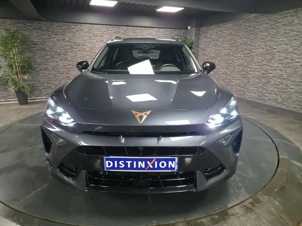 Vue avant d'un CUPRA Formentor gris métallisé avec phares allumés et logo cuivré sur le capot dans un showroom.