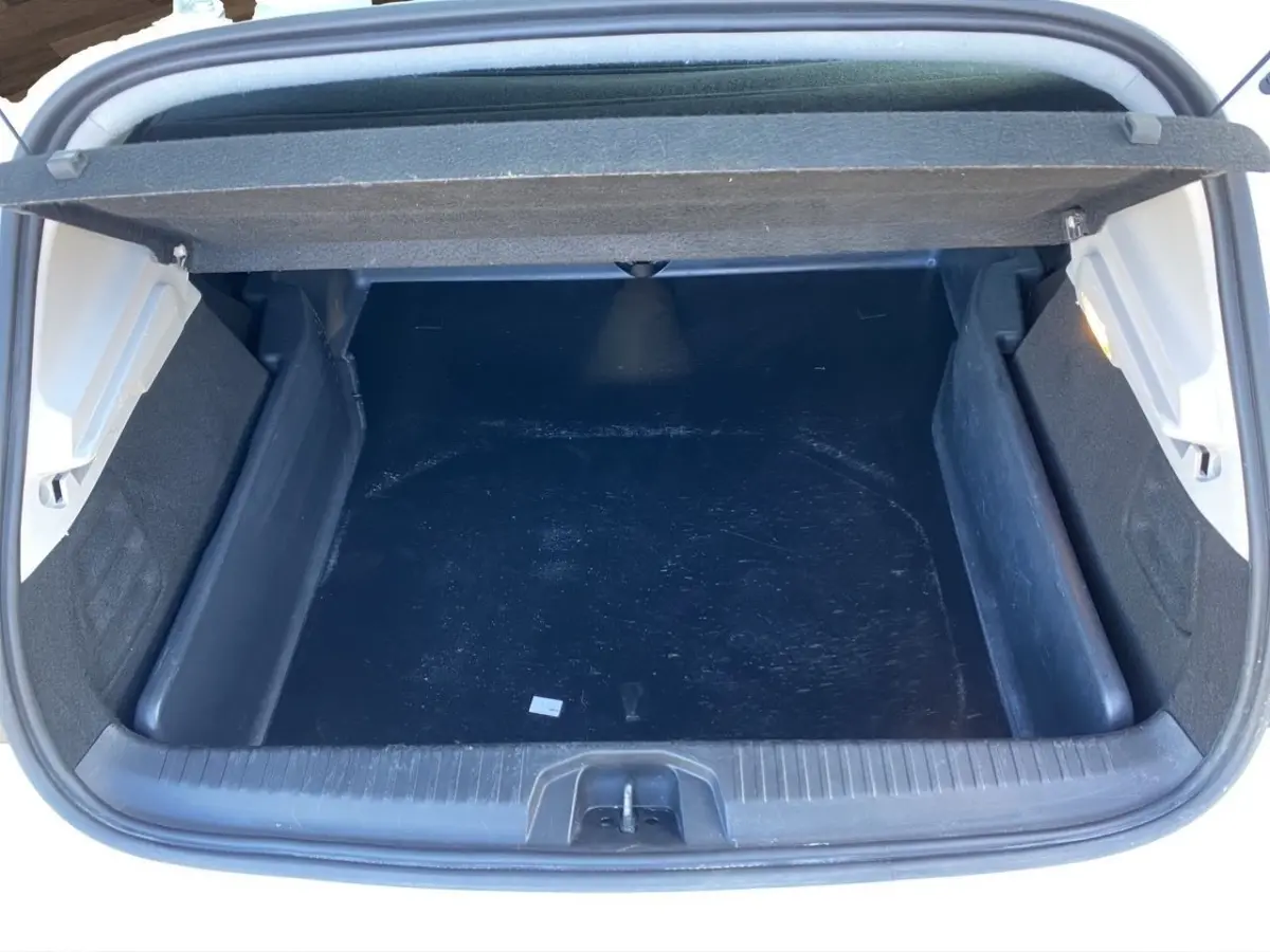 Vue plongeante sur le coffre ouvert d'une Renault Clio blanche, montrant un espace de chargement noir vide.