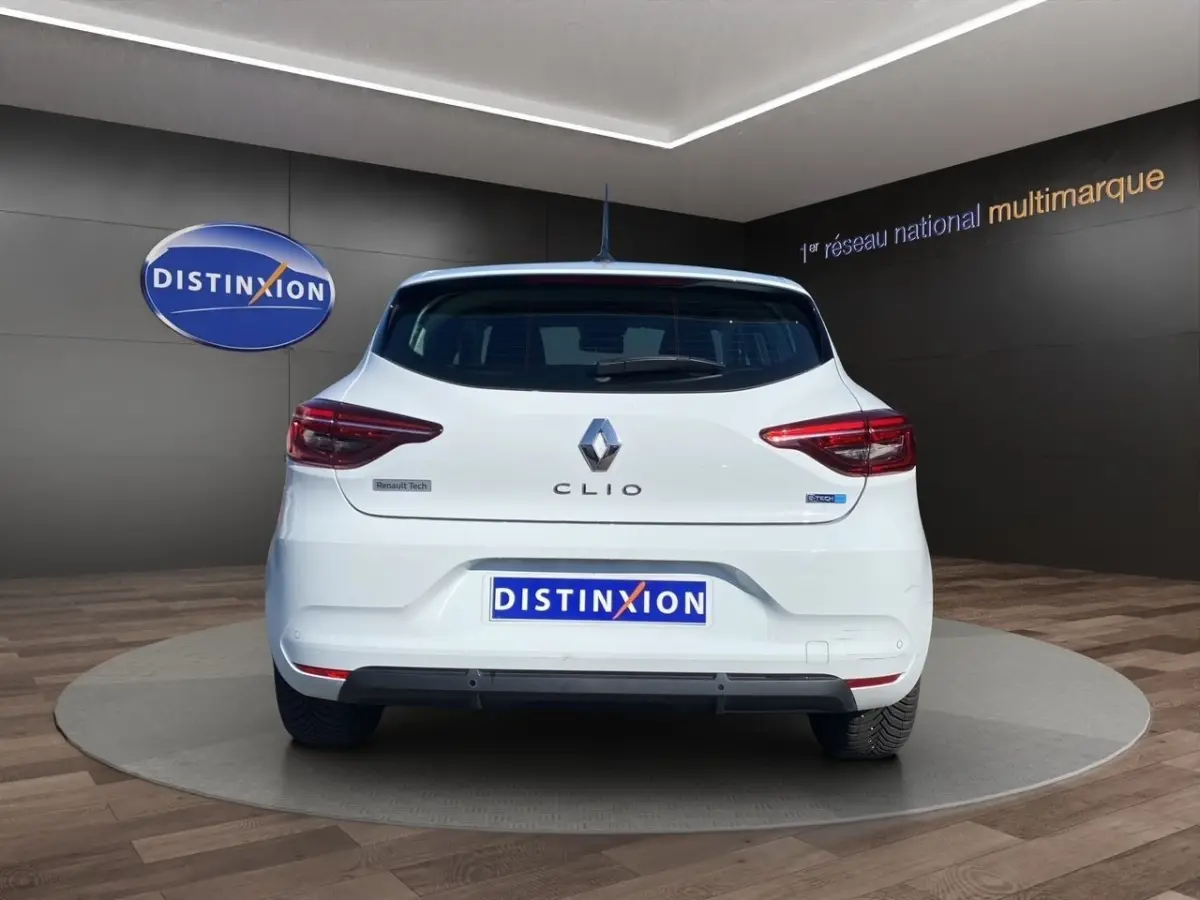 Vue arrière d'une Renault Clio blanche Business Réversible E-TECH 140 avec feux LED et logo visible sur fond showroom.