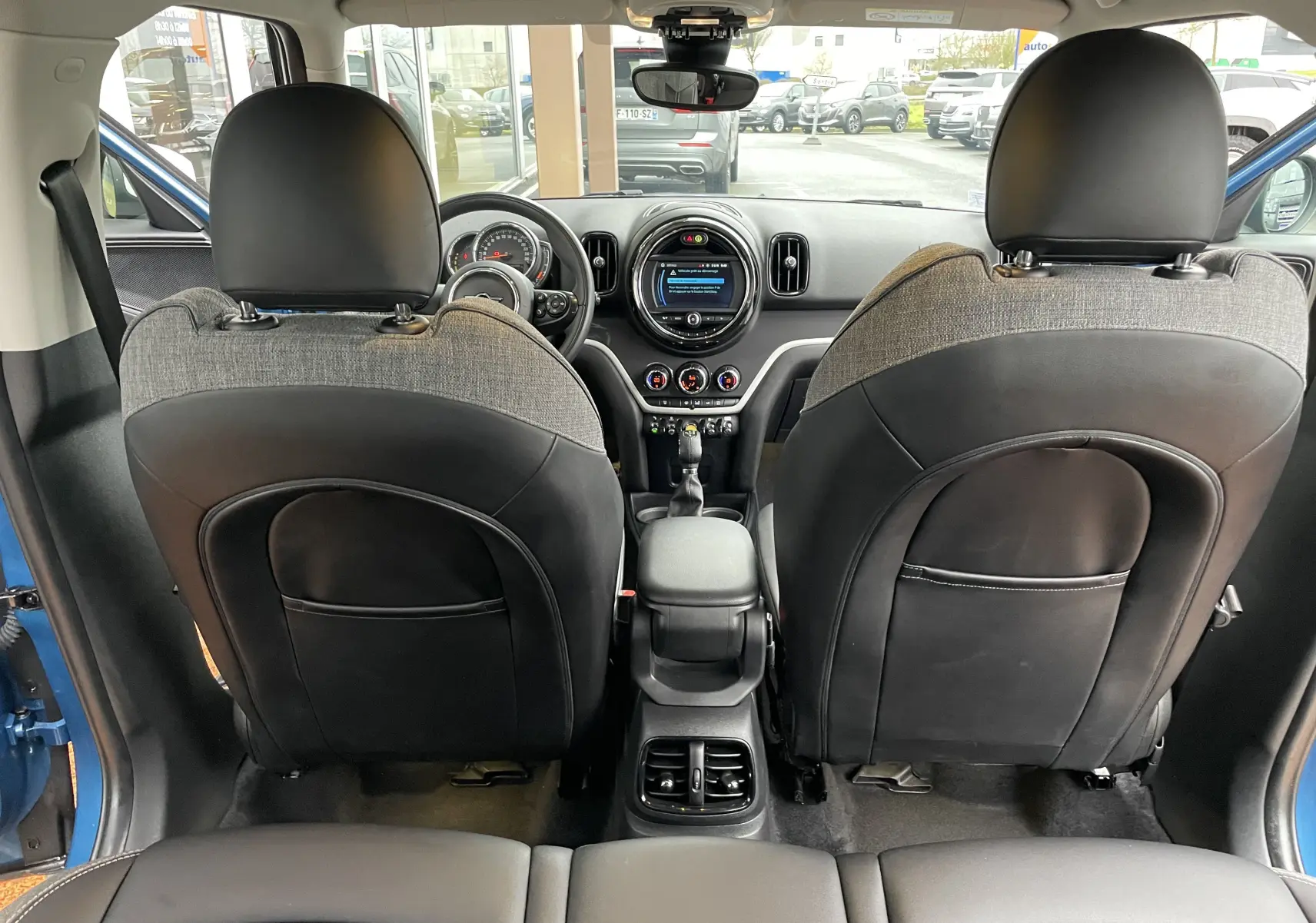 Intérieur vu depuis l'arrière d'une MINI Countryman bleu Island Metal, sièges tissu et cuir gris noir, tableau de bord moderne.