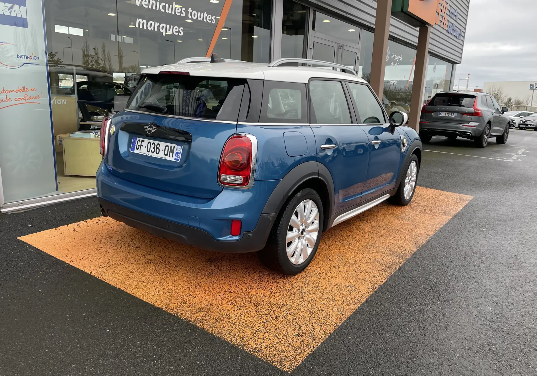 Vue 3/4 arrière droite d'une MINI Countryman Cooper S bleu Island Metal avec toit blanc, stationnée devant un showroom.