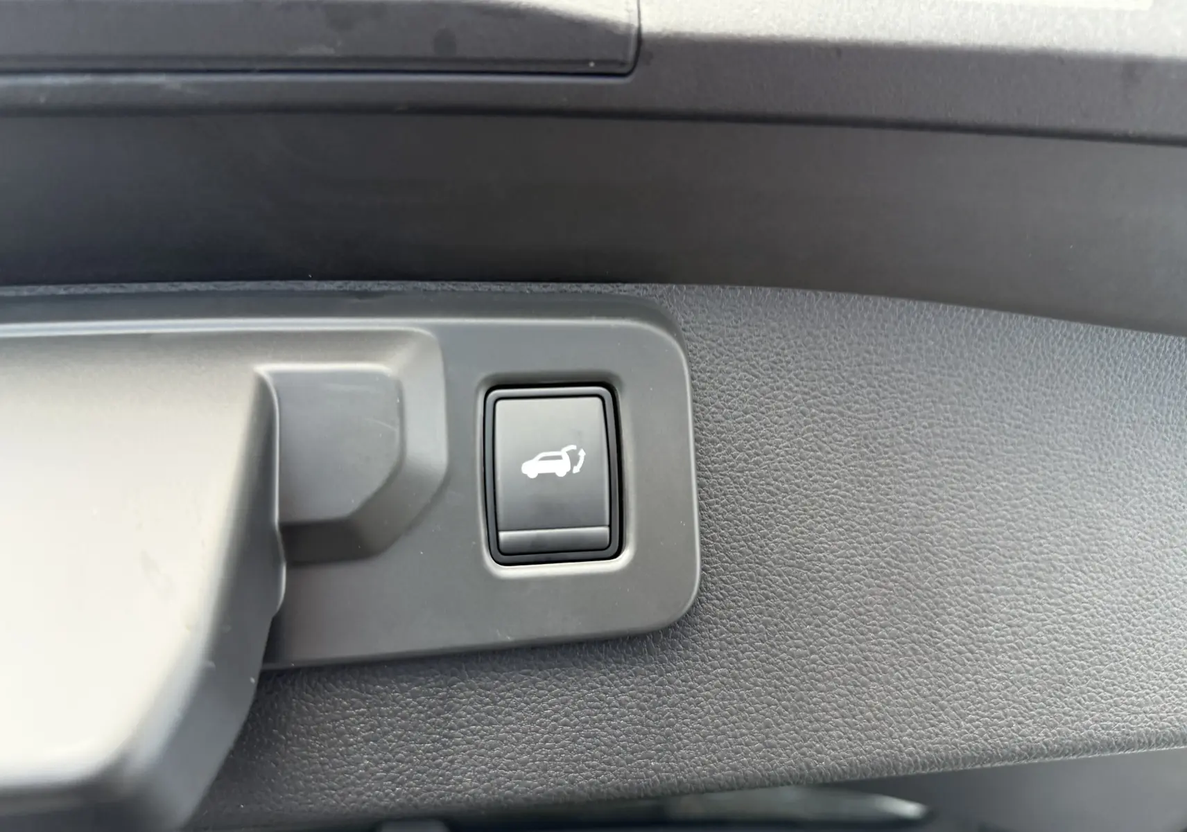 Gros plan sur le bouton d'ouverture du coffre dans l'habitacle du Renault Symbioz gris Rafale 2025.