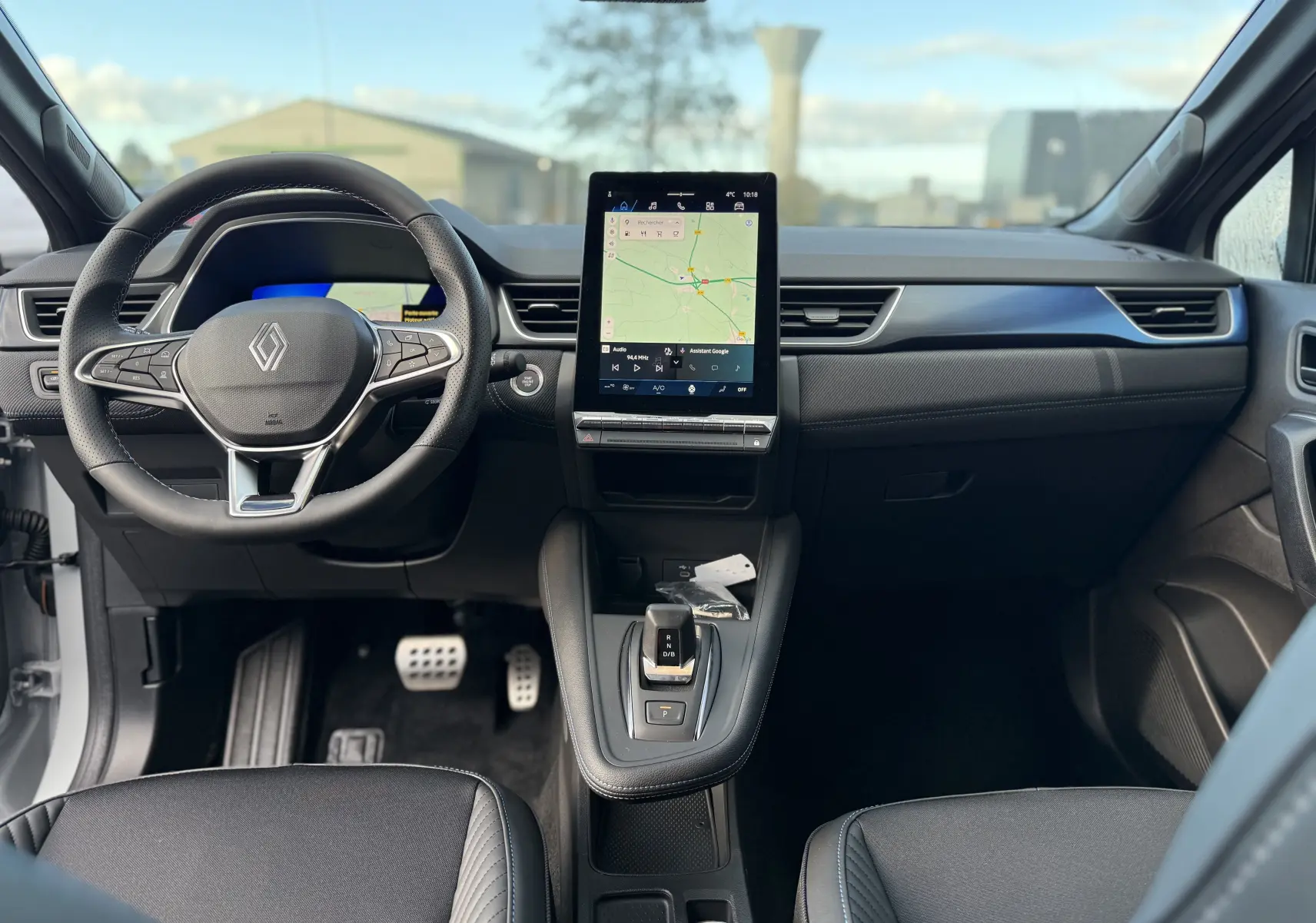 Vue intérieure frontale du tableau de bord et volant noir du Renault Symbioz gris Rafale avec écran tactile central affichant une carte.