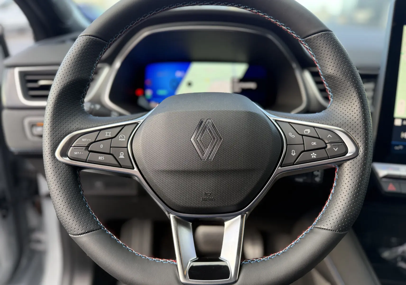 Gros plan sur le volant noir perforé avec surpiqûres tricolores et logo Renault au centre du Renault Symbioz gris Rafale 2025.