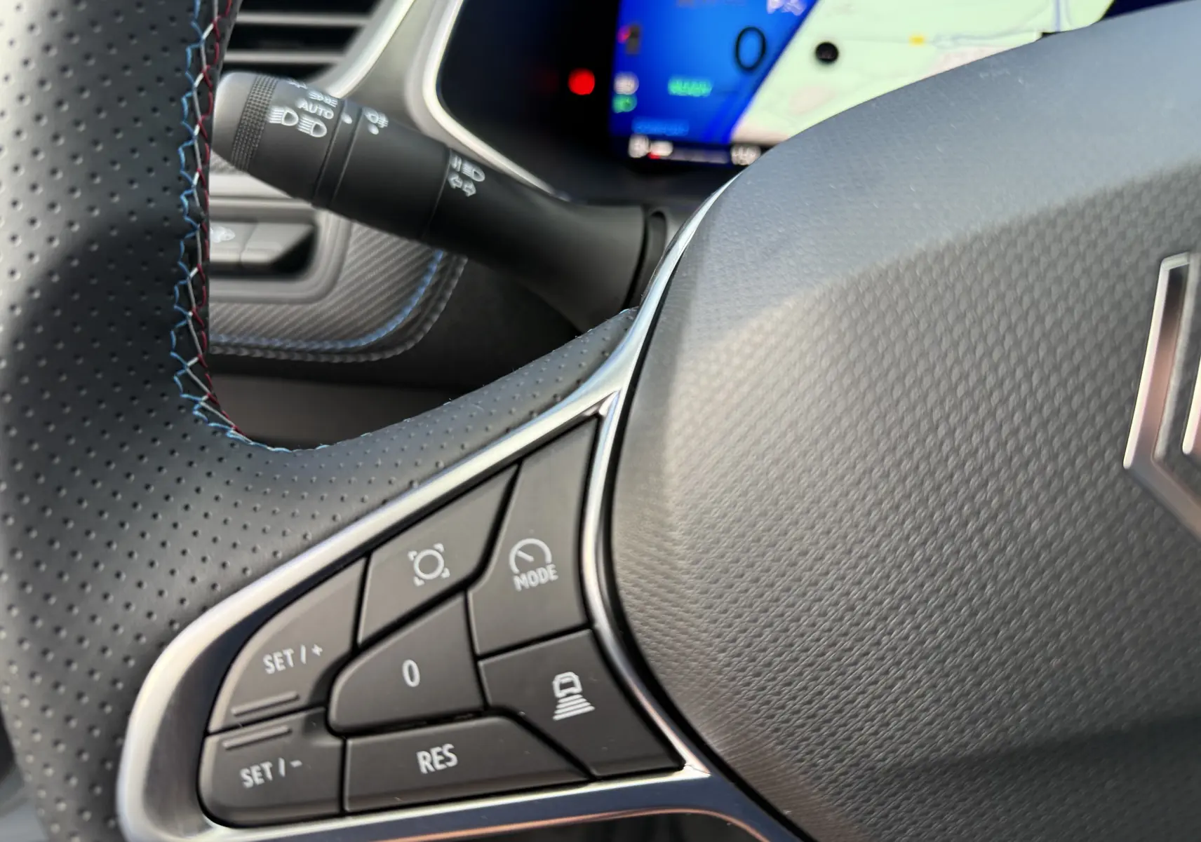 Gros plan sur le volant perforé gris du Renault Symbioz 2025 avec commandes multifonctions et écran numérique en arrière-plan.