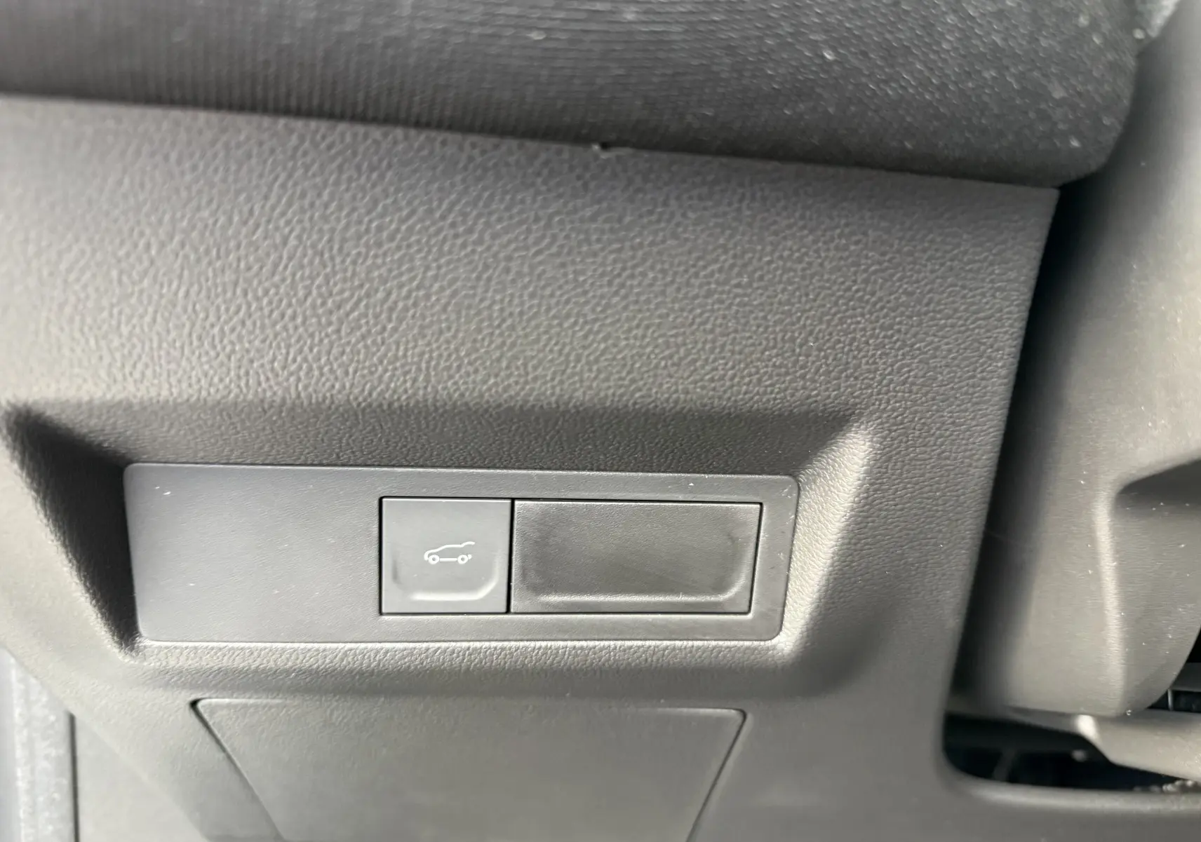 Gros plan sur le bouton d'ouverture du coffre dans l'habitacle du Renault Symbioz gris Rafale, version hybride 2025.