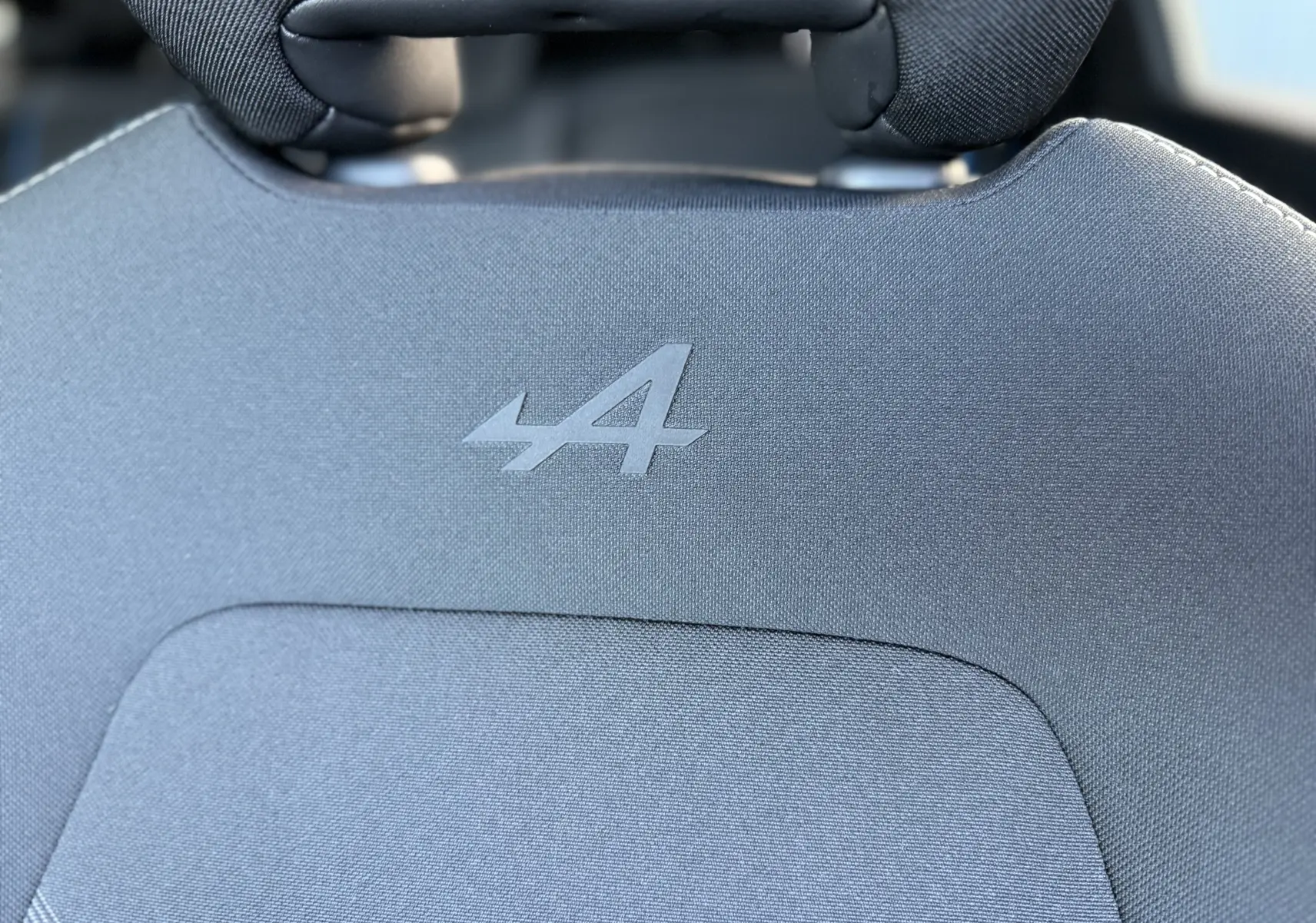 Gros plan sur le logo Alpine embossé sur l'appui-tête en tissu gris du siège avant du Renault Symbioz 2025.