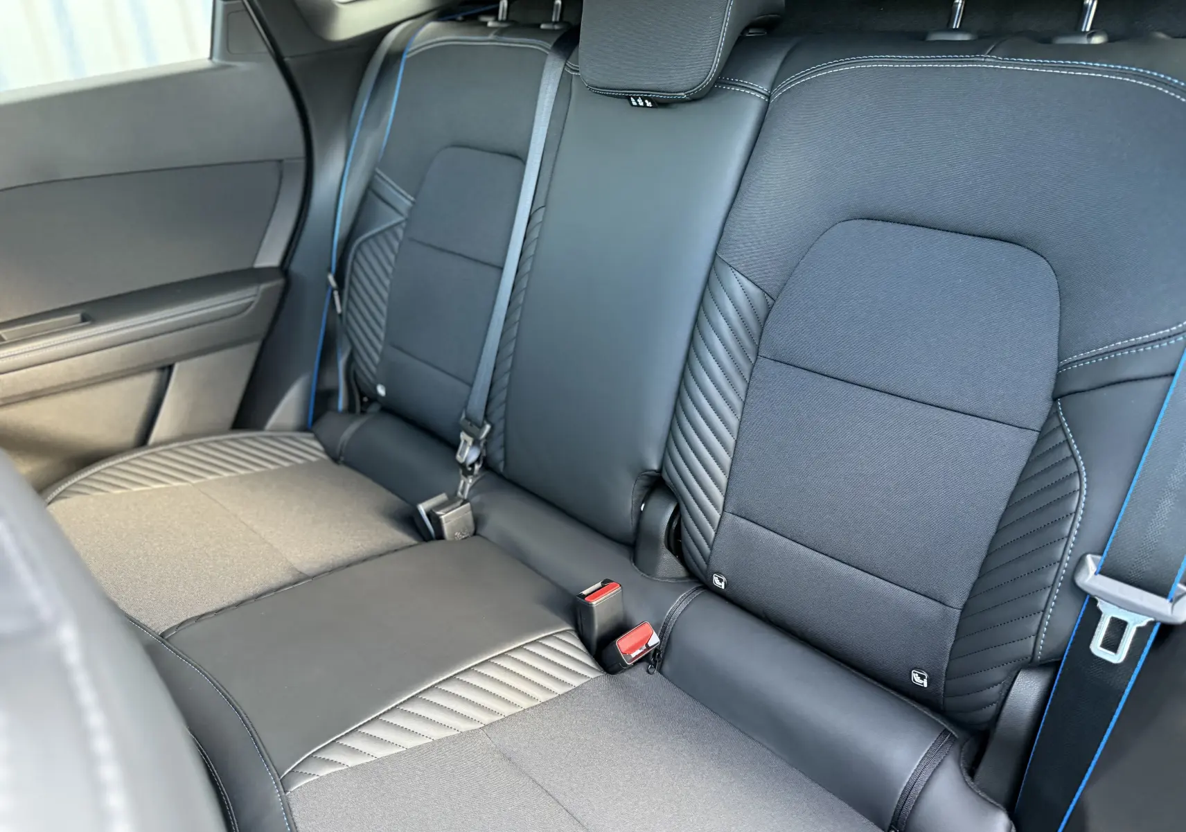 Vue rapprochée des sièges arrière noirs et gris du Renault Symbioz 2025 avec surpiqûres bleues et ceintures assorties.