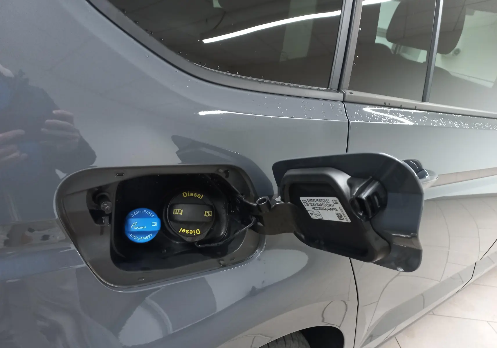 Vue rapprochée du côté gauche arrière du Volkswagen Touran gris Dauphin avec trappe à carburant ouverte montrant les bouchons Diesel et AdBlue.