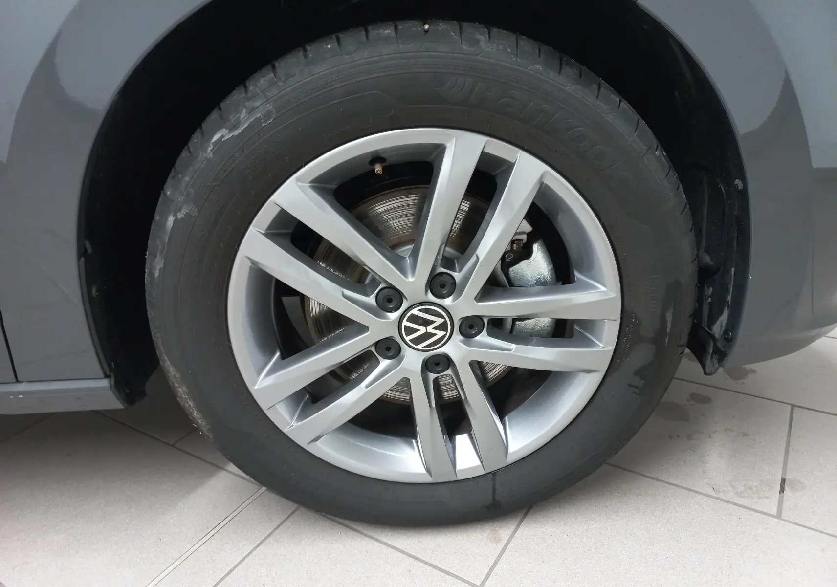 Gros plan sur la roue avant droite du Volkswagen Touran gris dauphin avec jante alliage à dix branches.