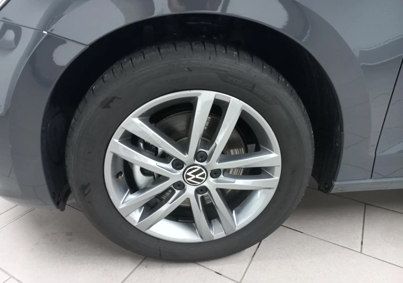 Gros plan sur la roue avant gauche du Volkswagen Touran gris dauphin avec jante alliage à 5 doubles branches.