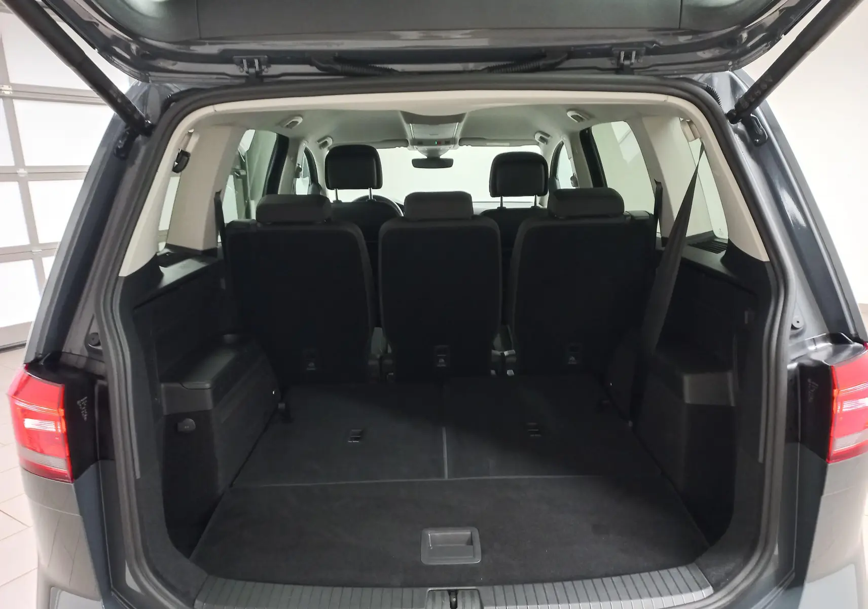 Vue arrière du coffre ouvert du Volkswagen Touran 2025 gris Dauphin, montrant les sièges arrière et l'espace de chargement.