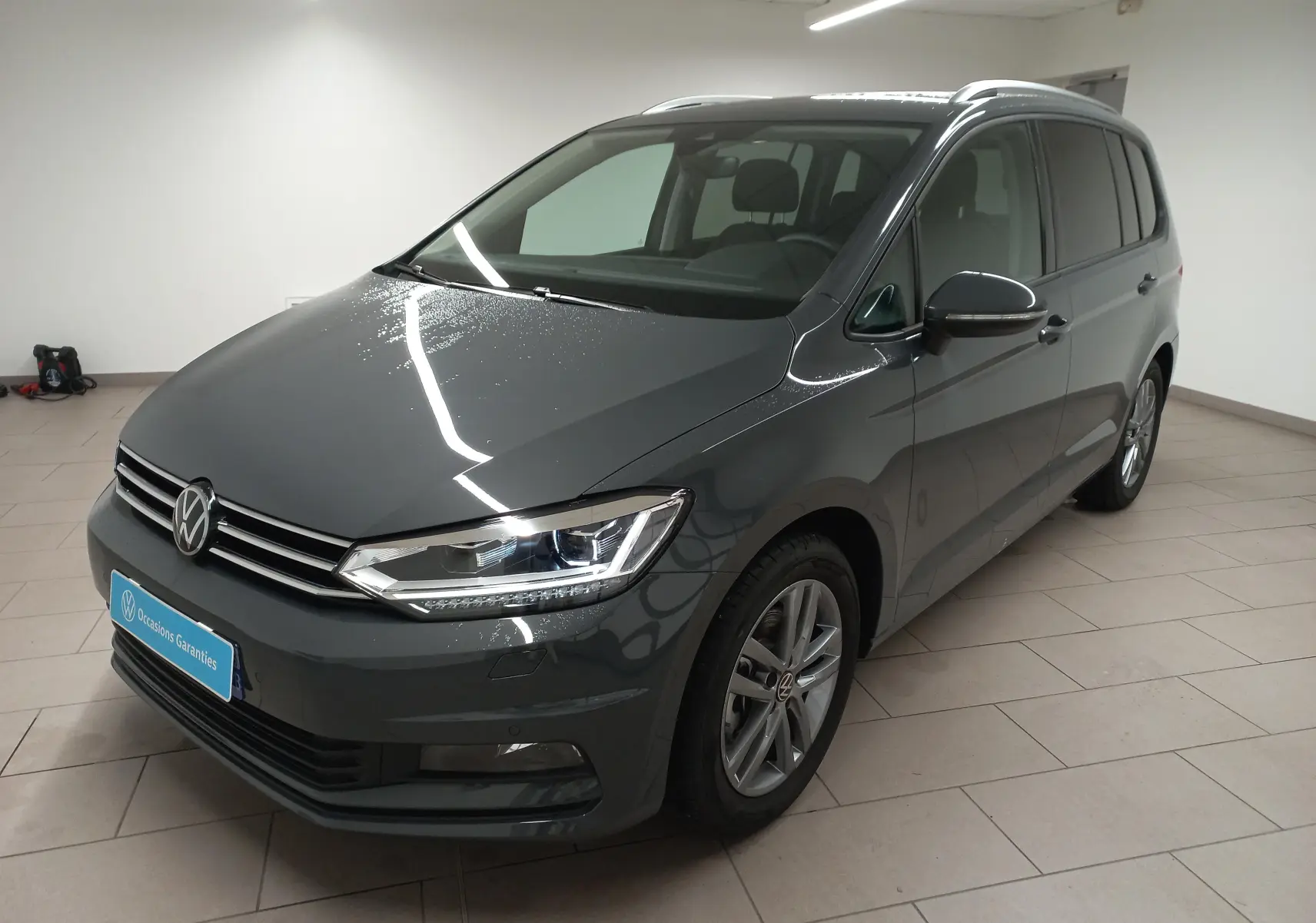 Volkswagen Touran 2025 gris dauphin en 3/4 avant droit, avec phares LED et jantes alliage visibles.