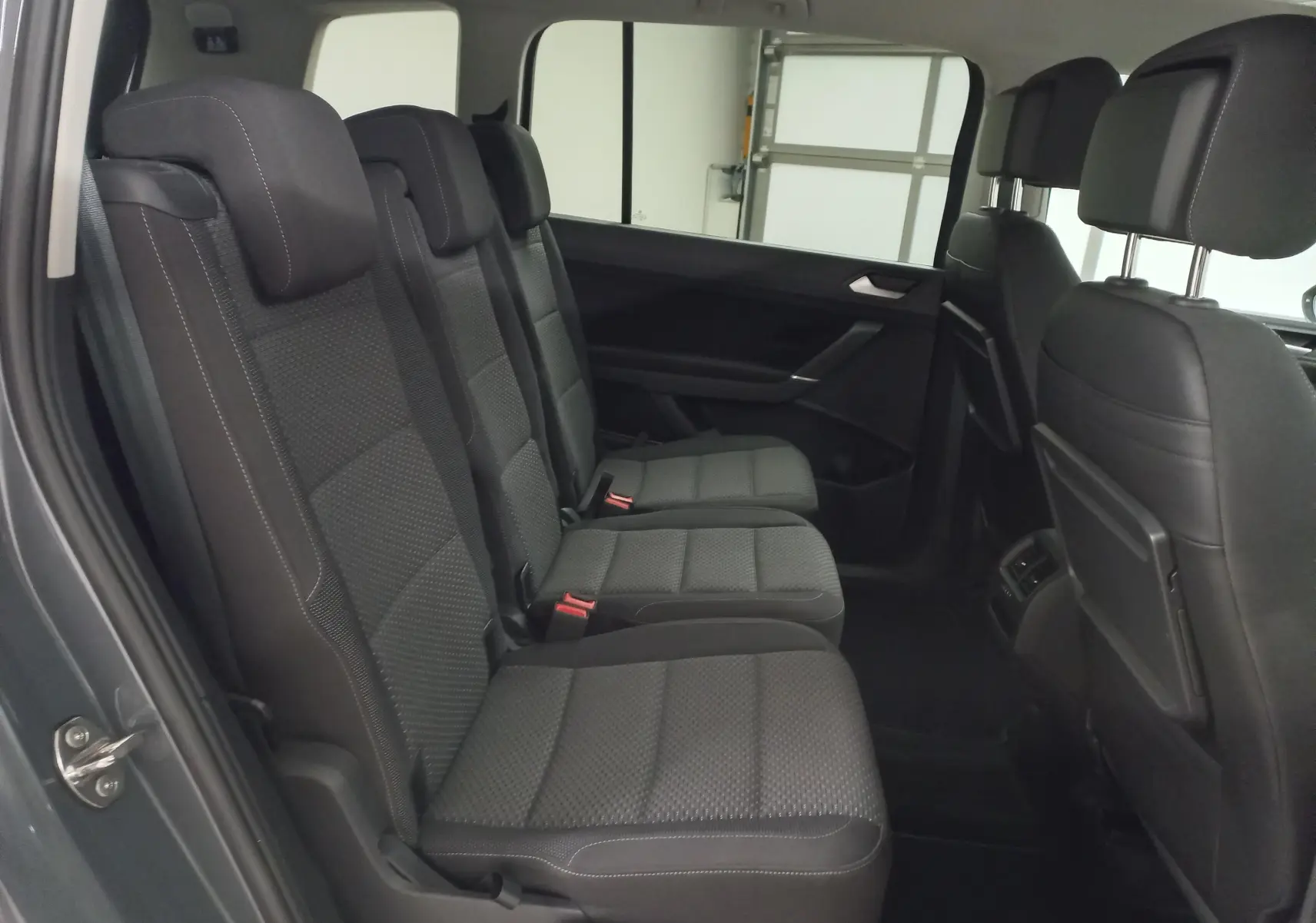 Vue intérieure côté gauche des sièges arrière en tissu gris foncé du Volkswagen Touran 2025, version 7 places.
