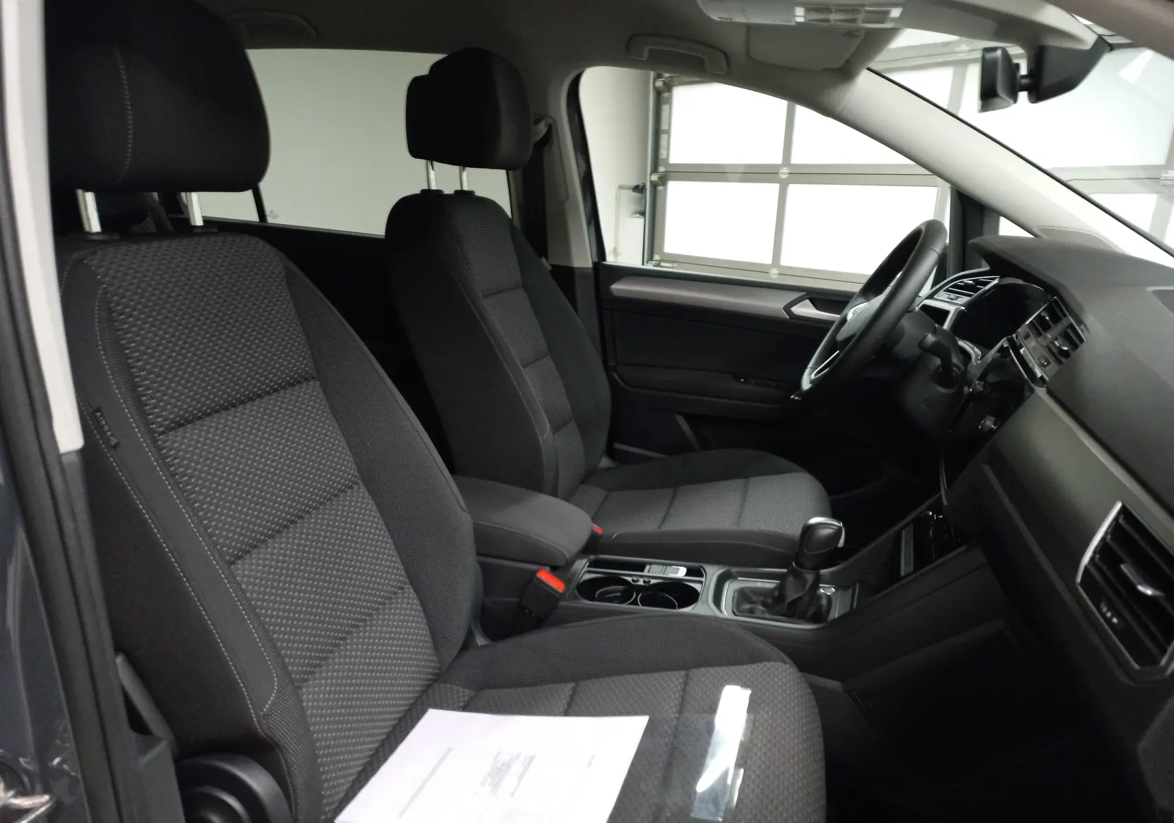 Vue intérieure côté gauche du Volkswagen Touran 2025 gris dauphin, montrant les sièges avant et la console centrale.