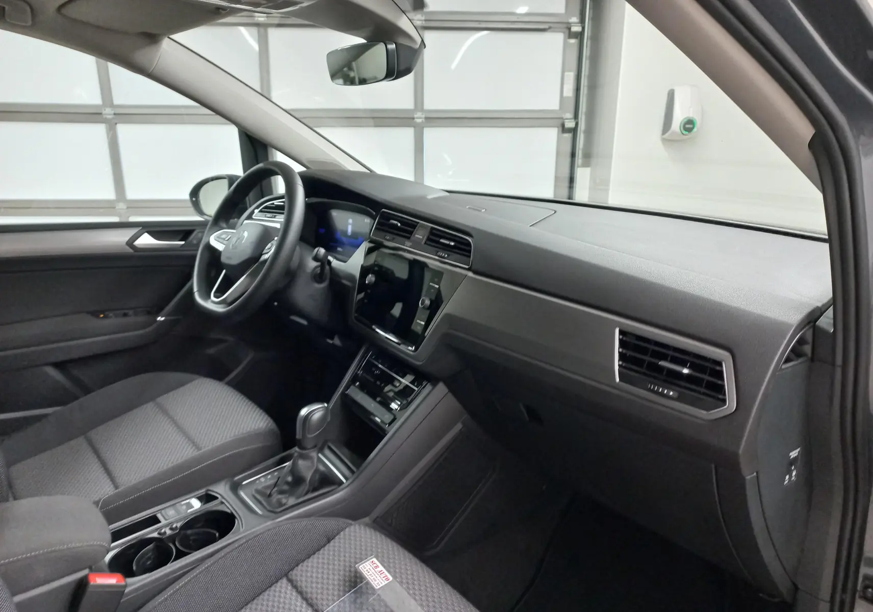 Vue intérieure côté conducteur du Volkswagen Touran 2025 gris dauphin, avec tableau de bord moderne et boîte automatique.