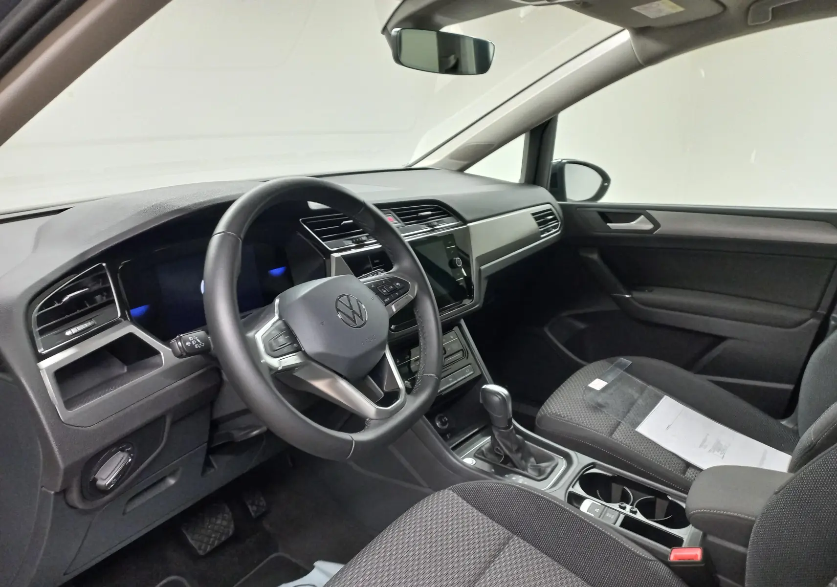 Vue intérieure côté conducteur du Volkswagen Touran 2025, tableau de bord moderne avec volant multifonction et console centrale.