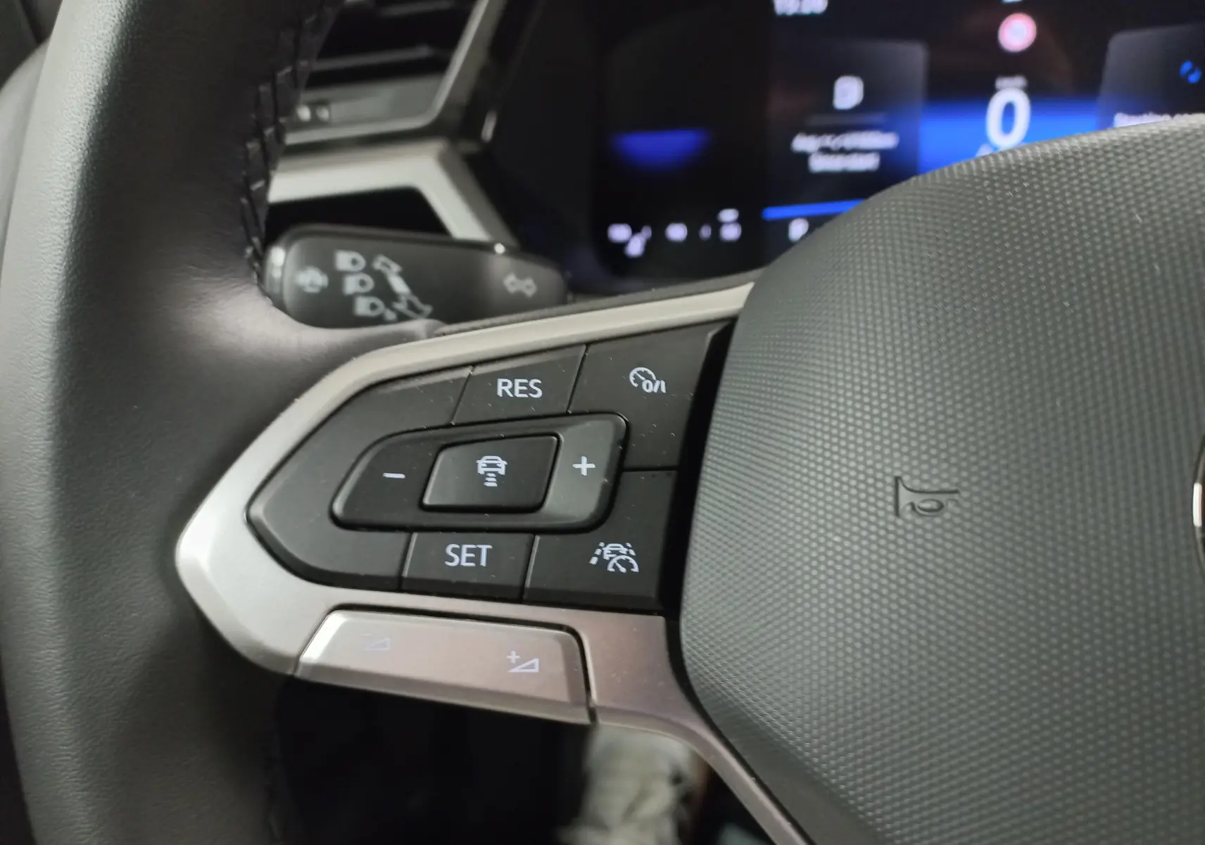 Gros plan sur les commandes gauche du volant noir du Volkswagen Touran 2025, avec affichage digital en arrière-plan.