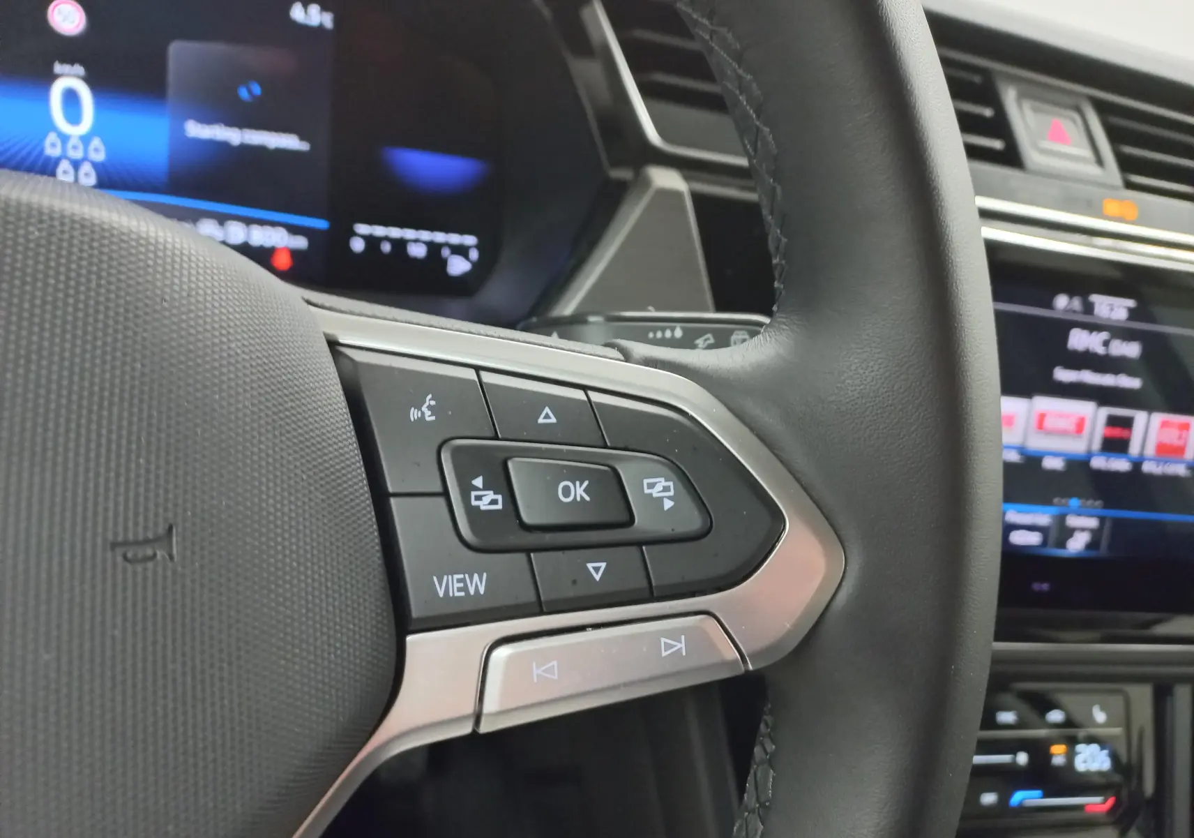 Gros plan sur les commandes au volant du Volkswagen Touran 2025, avec tableau de bord numérique et écran tactile en arrière-plan.