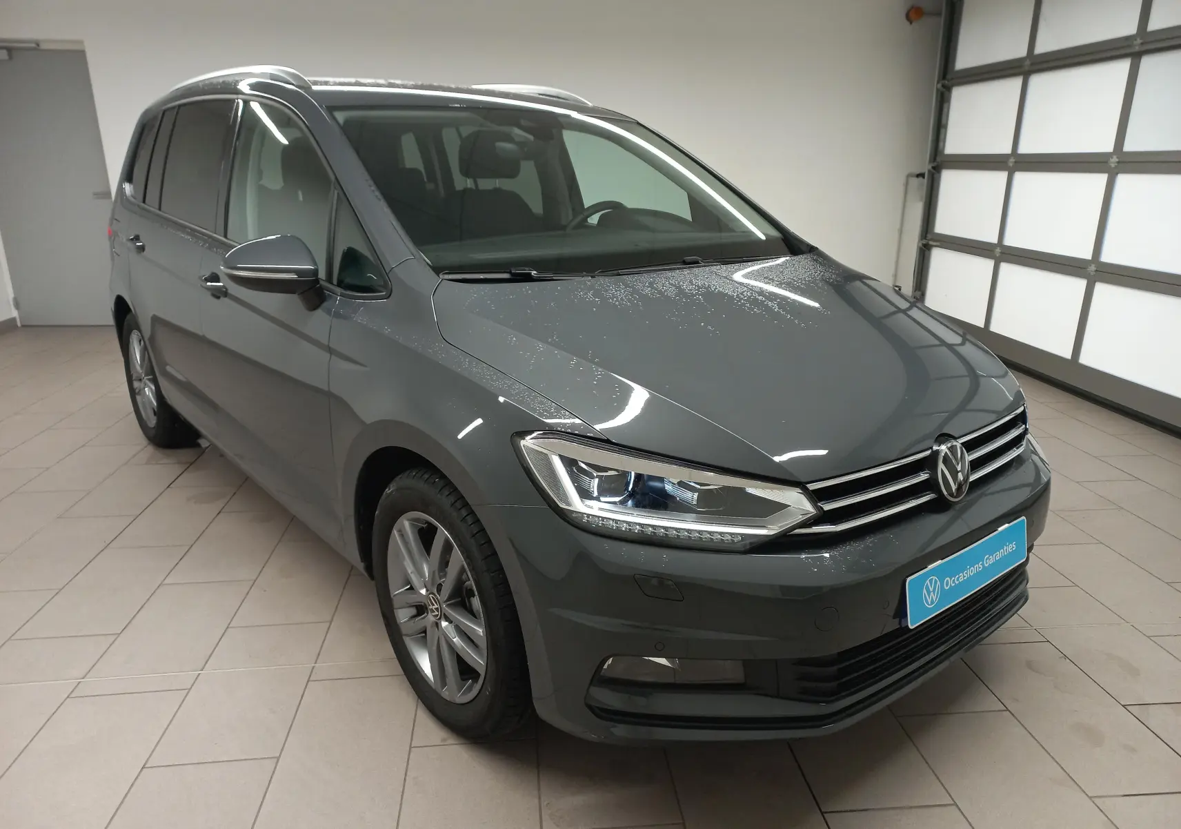 Volkswagen Touran 2025 gris dauphin en 3/4 avant droit, avec phares LED et jantes alliage visibles.