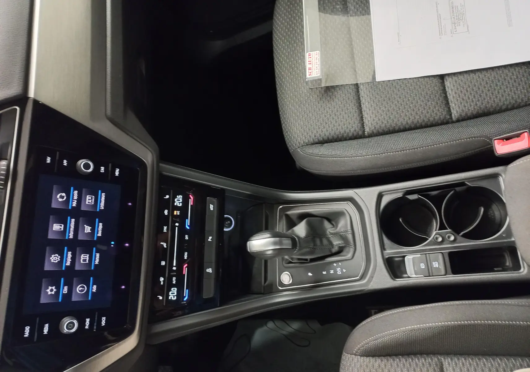 Vue intérieure centrée sur la console centrale du Volkswagen Touran 2025 avec levier de boîte auto et sièges gris.