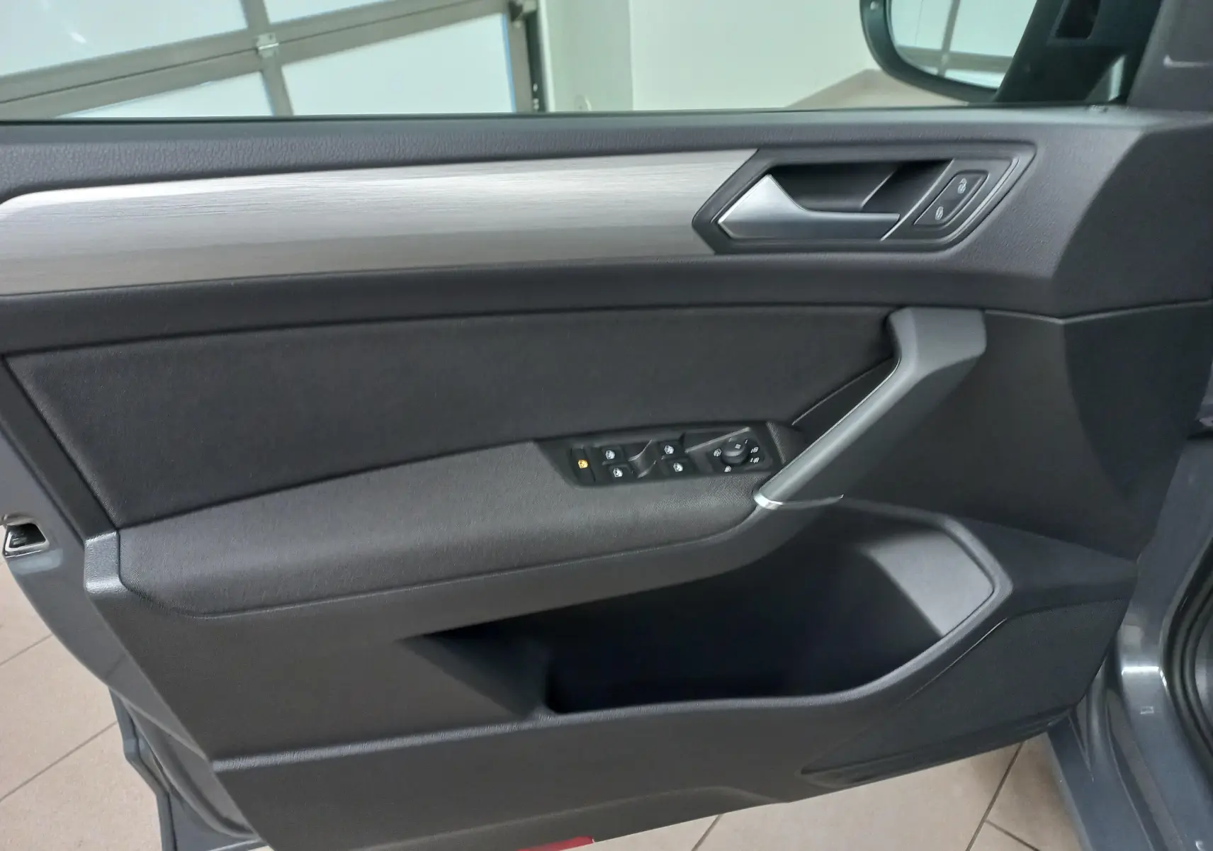 Vue intérieure du panneau de porte côté conducteur du Volkswagen Touran gris dauphin, avec commandes électriques et insert décoratif gris.