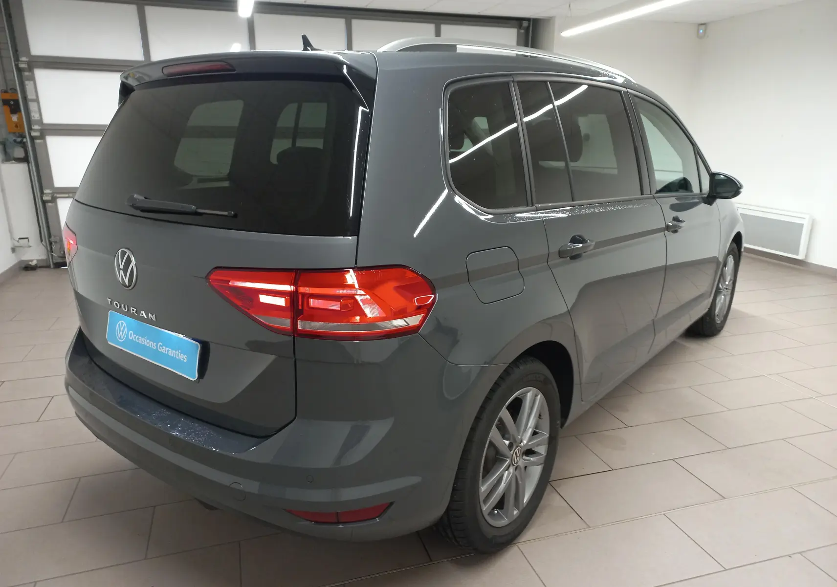 Vue 3/4 arrière droite d'un Volkswagen Touran 2025 gris dauphin métallisé, avec vitres teintées et jantes alliage.