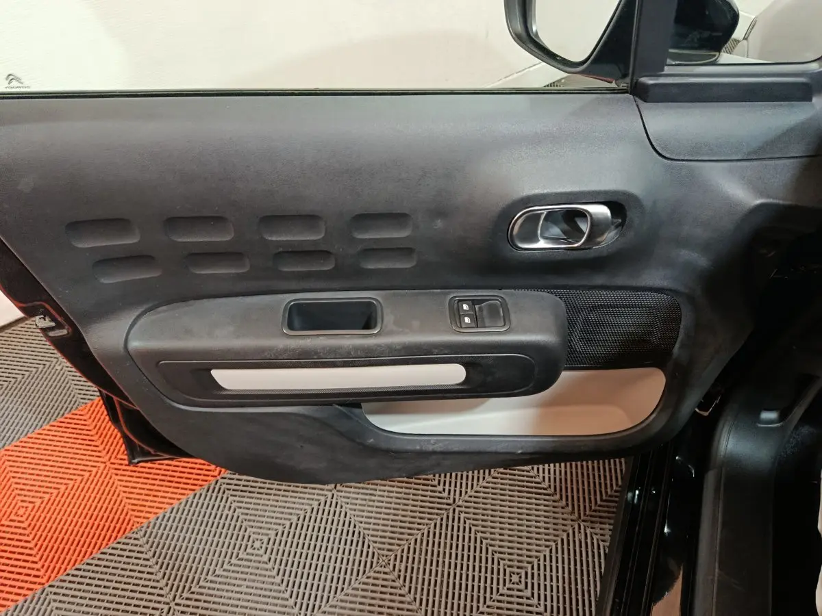 Vue intérieure côté gauche de la porte noire de la Citroën C3 2024 avec poignée chromée et commandes électriques.