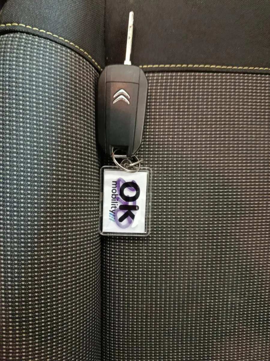 Clé de voiture Citroën posée sur un siège tissu noir à motifs gris avec surpiqûres jaunes visibles.