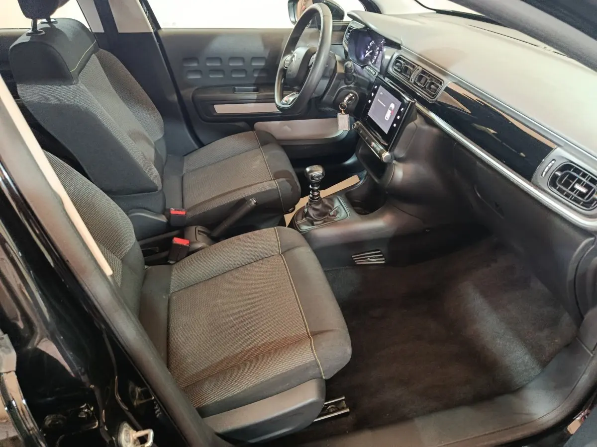 Vue intérieure côté conducteur de la Citroën C3 noire 2024, montrant sièges tissu, tableau de bord avec écran tactile et volant multifonctions.