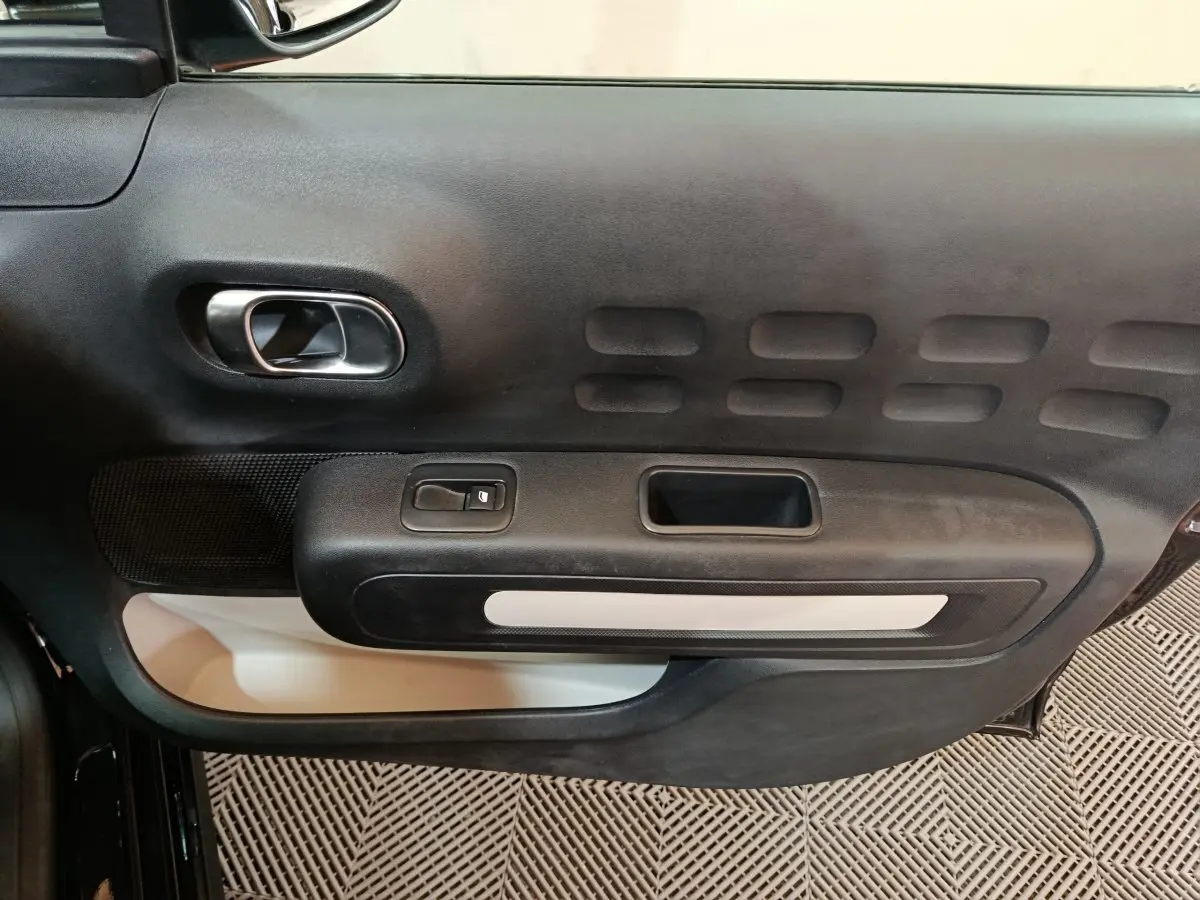 Vue rapprochée de la porte intérieure côté conducteur de la Citroën C3 noire avec poignée argentée et commande de vitre.