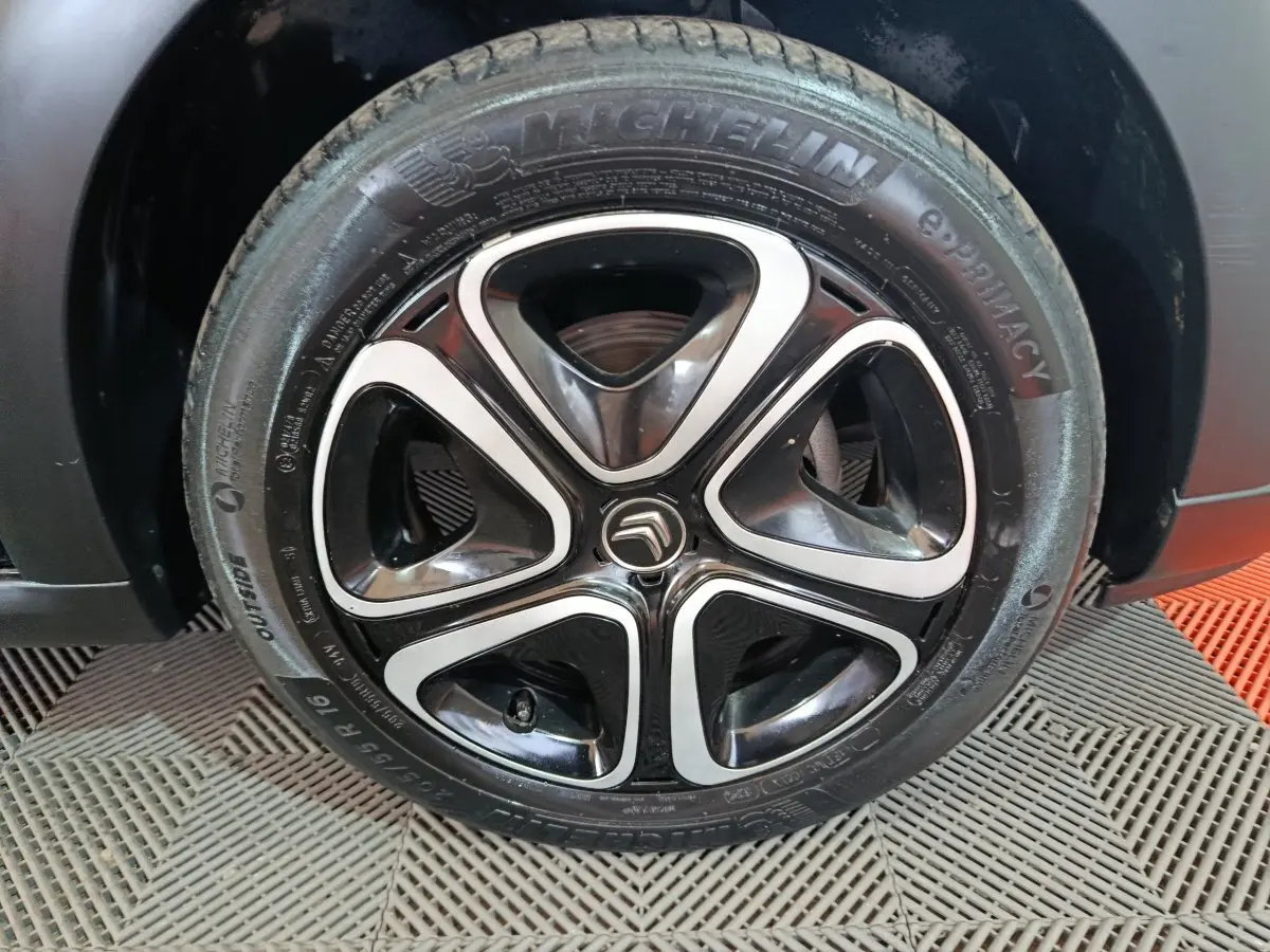 Gros plan sur la jante noire et argentée avec logo Citroën d'une roue Michelin d'une Citroën C3 noire 2024.