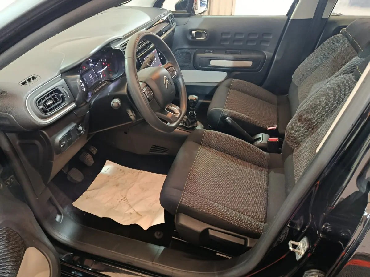 Intérieur avant droit de la Citroën C3 noire 2024, volant multifonctions, tableau de bord digital et sièges tissu gris.